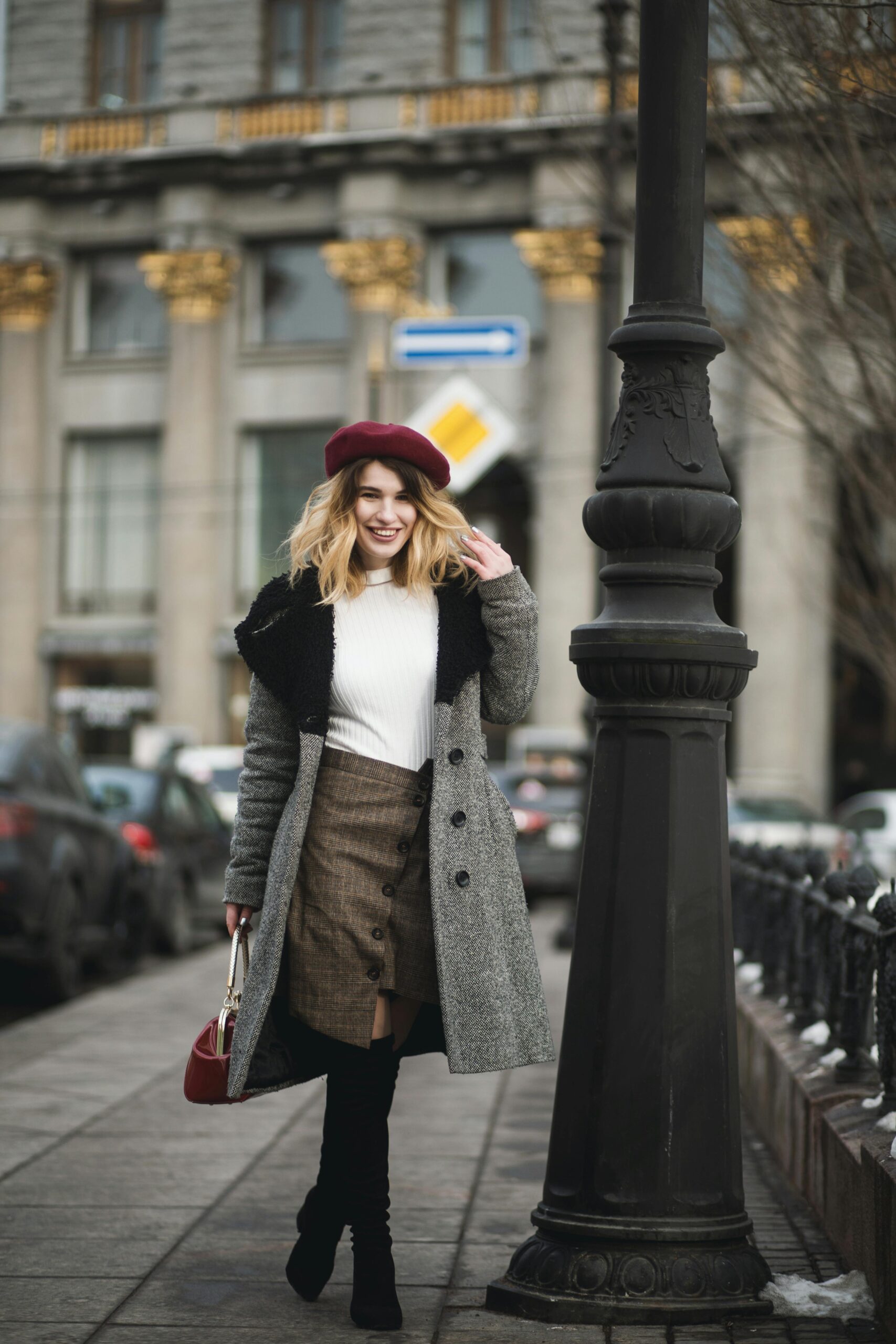 Stylish woman in coat and beret walking in city street, showcasing urban winter fashion.